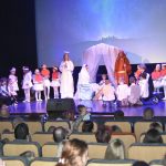 Grupa dorosłych i dzieci w strojach jasełkowych wystepuje na scenie.