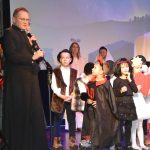 Grupa dzieci w strojach jasełkowych oraz męzczyzna ubrany w sułtanne na scenie.