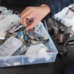 Osoba sięgająca do pudełka z częściami elektronicznymi.