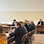 Grupa dorosłych osób w oficjalnych strojach siedzacych na sali obrad przy biurkach.