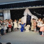 Grupa dzieci podczas przedstawienia jasełkowego. W centrum znajduje się żłobek i dziewczynka przebrana za Marię.