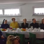 Grupa dorosłych w tym zakonnic zasiadających przy podłużnym stole.