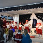 Dzieci w czasie wystąpienia jasełkowego. Tańczą w biało-czerwonych mikołajkowych strojach. Oglądaję je dzieci oraz dorośli.