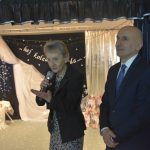 Dorosły mężczyzna oraz starsza kobieta przemawiająca za pomocą mikrofonu.