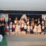 Grupa dorosłych i dzieci pozujących do zdjęcia na sali. Z tyłu widać ozdoby świąteczne. Dzieci trzymają dyplomy.