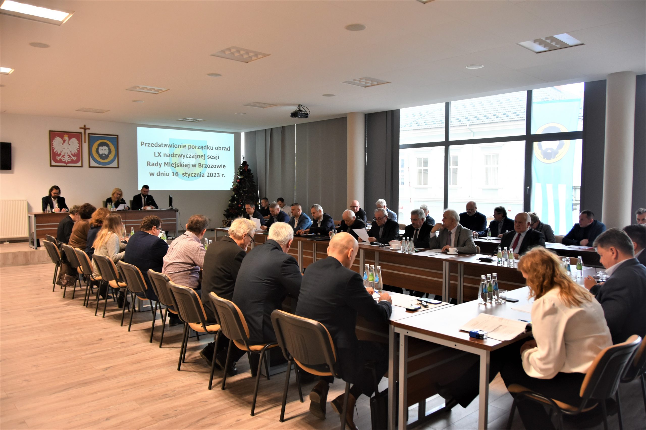 Grupa dorosłych osób różnej płci i wieku zasiadająca na dużej sali konferencyjnej.