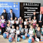 Grupa dzieci dorosłych i dzieci pozujących z upominkami, medalami i statuetkami.