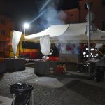 Namiot biały na rynku, w nim stoją męźczyzni ubranui w stroje strażackie i grilują kielbasę.