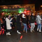 Grupa młodych osób tańczy przed sceną na rynku.