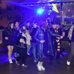 Grupa młodych osób tańczy przed sceną na rynku.