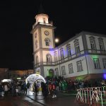 Grupa osób stoi przed budynkiem ratusza i słucha koncertu.