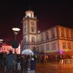 Grupa osób stoi przed budynkiem ratusza i słucha koncertu.