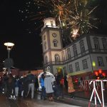 Grupa osób stoi przed budynkiem ratusza i oglądają fajerwerki nad ratuszem.