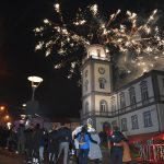 Grupa osób stoi przed budynkiem ratusza i oglądają fajerwerki nad ratuszem.