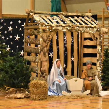Drewniana szopka na sali gimnastycznej. Siedzi w niej dwójka dzieci przebranych za Maryję i Józefa.