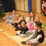 Grupa dzieci różnej płci siedząca na sali gimnastycznej w strojach jasełkowych.