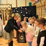 Kobieta przekazuje dzieciom na sali gimnastycznej podarki.