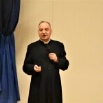 Mężczyzna ubrany w sutannę przemawia do mikrofonu.