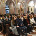 Grupa ludzi siedzi w ławkach brązowych w kościele.