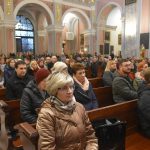 Grupa ludzi siedzi w ławkach brązowych w kościele.