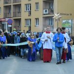 Barwny korowód idzie ulicami. Na przodzie idzie młody chłopak z niebieskiej kurtce i trzyma złotą gwiazdę.