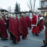 Grupa osób ubrana w czerwone szaty idzie w przemarszu na ulicy.