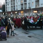 Grupa osób dorosłych i dzieci ubranych w zimowe kurtki idzie w przemarszu po ulicy.