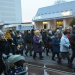 Grupa osób dorosłych i dzieci ubranych w zimowe kurtki idzie w przemarszu po ulicy.