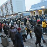 Grupa osób dorosłych i dzieci ubranych w zimowe kurtki idzie w przemarszu po ulicy.