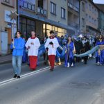 Gruap osób siedzi w przemarszu na ulicy. Na przodzie chłopak w niebieskiej kurtce ze złotą gwiazdą.