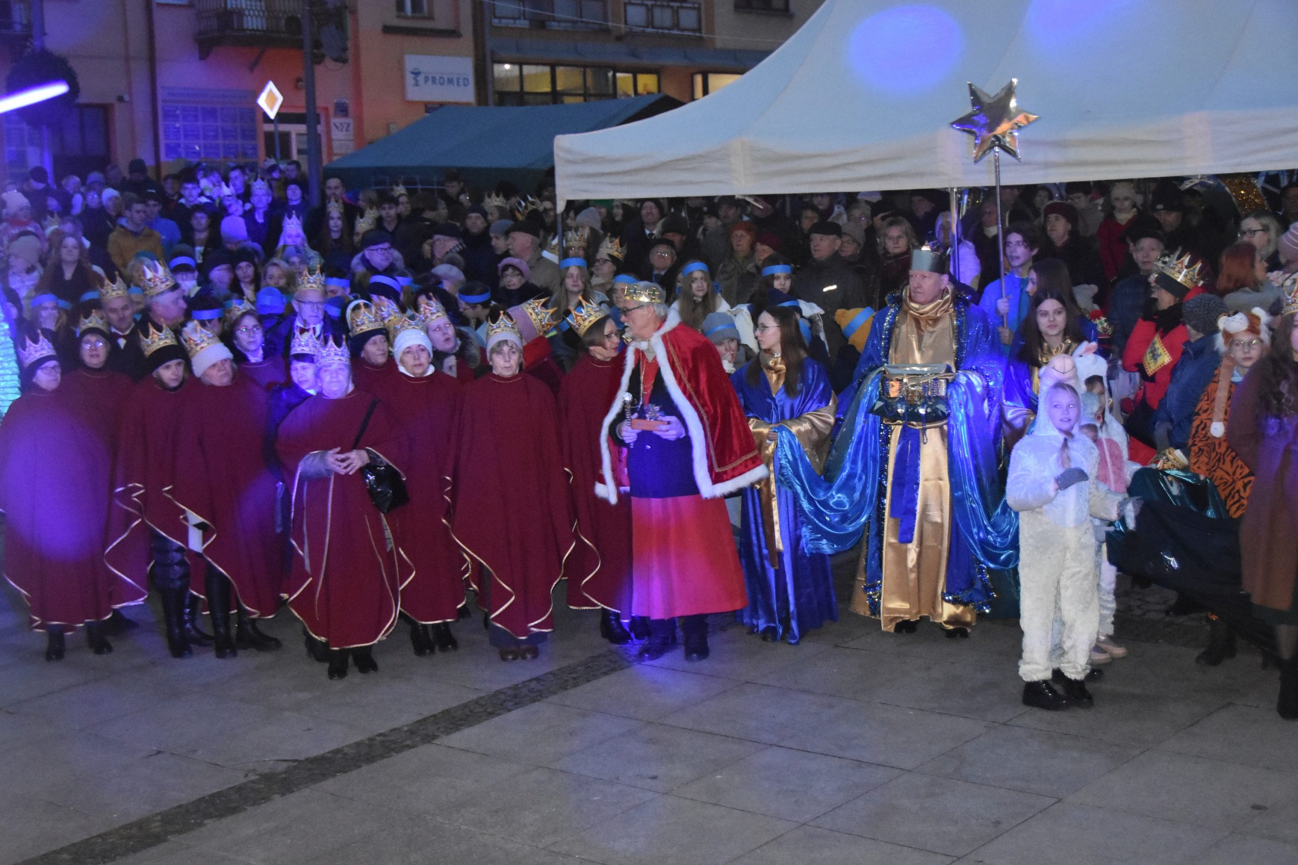 Grupa osób stoi na rynku podczas wydarzenia imprezowego.