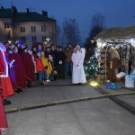 Grupa osób ubranych na czerwono składa dary do szopki.