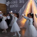 Dziewczynki przebrane w białe spódniczki i koszulki tańczą na sali przedszkolnej