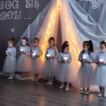 Dziewczynki przebrane w białe spódniczki i koszulki tańczą na sali przedszkolnej