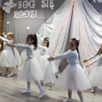 Dziewczynki przebrane w białe spódniczki i koszulki tańczą na sali przedszkolnej