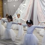 Dziewczynki przebrane w białe spódniczki i koszulki tańczą na sali przedszkolnej