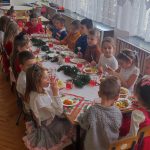 Dzieci ubrane odświętnie jedzą dania wigilijne.