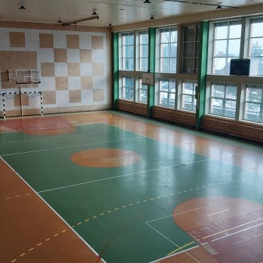 Widok na rozległą salę gimnastyczną. Na jednej ze ścian znajdują sie okna.