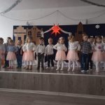 Grupa dzieci w czasie przedatwienia jasełkowego. Stoją na podescie i pozują w rzędzie do zdjęcia.