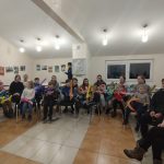 Duża grupa młodzieży siedząca w rozległej sali. W rękach trzymają nadmuchane balony.