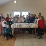 Grupa dzieci pozujących do zdjęcia. przed nimi znajduje się stół z ręcznie wykonanymi ozdobnymi kartkami.