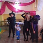 Grupa dzieci i dorosłych stojąca w strojach karnawałowych na sali.