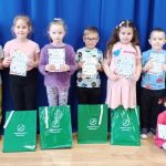 Grupa dzieci, dziewczynek i chłopców stoją w sali, na tle granatowej zasłony i trzymają w rękach dyplomy.