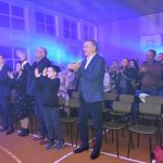 Grupa ludzi stoi na sali i klaszcze w dłonie.