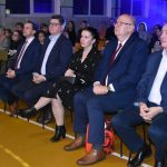 Grupa ludzi siedzi na krzesełekach i ogląda przedstawienie.