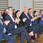 Grupa ludzi kobiet i mężczyzn siedzi na krzesełkach na sali i klaszcze w dłonie bijąc brawo.