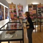 Starsza kobieta w okularach ogląda wystawę w muzuem.