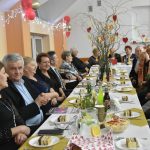 Grupa starszych osób obydwu płci zasiadająca przy podłużnych stołach bankietowych.