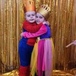 Chłopak i dziewczynka w w wieku przedszkolnym strojach karnawałowych pozujących do zdjęcia przed złotą zasłoną.