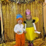 Chłopak i dziewczynka w wieku przedszkolnym w strojach karnawałowych pozujących do zdjęcia przed złotą zasłoną.